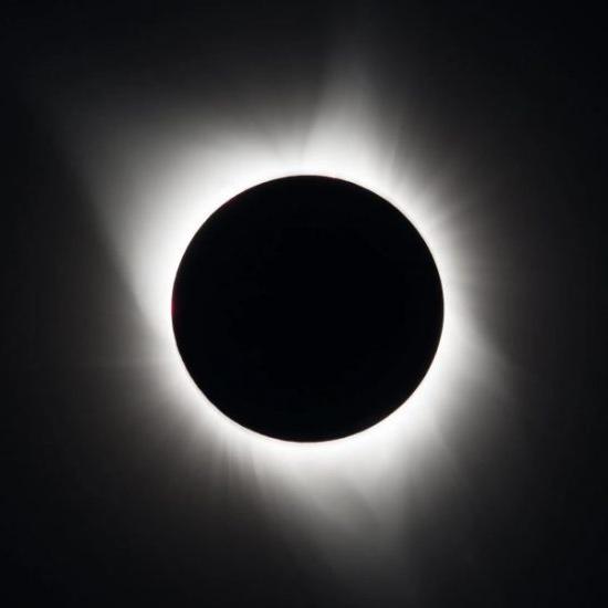 A total solar eclipse showing a darkened sun with a bright, glowing corona around its edges.